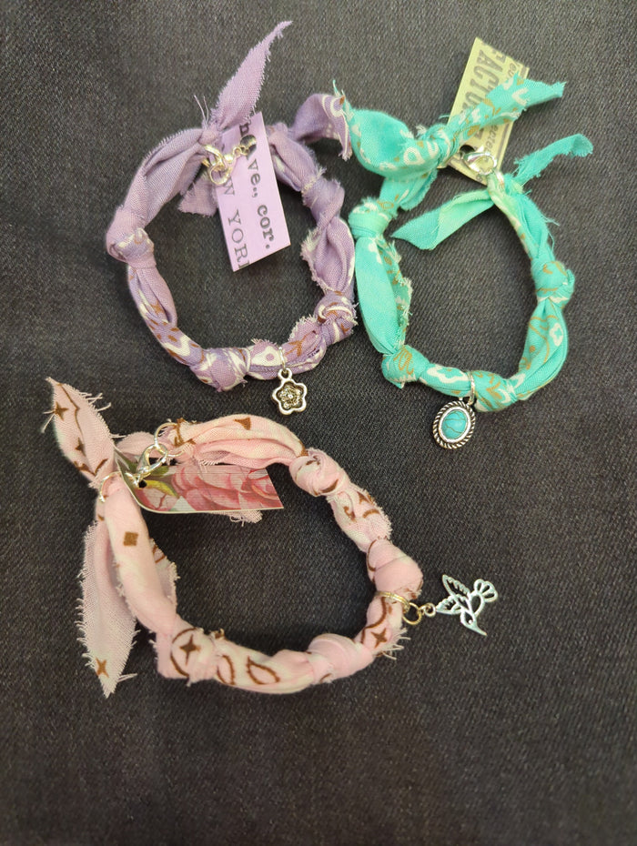 Wildwood Botanicals bandana charm bracelet with colorful fabric band and decorative charms on a neutral background.