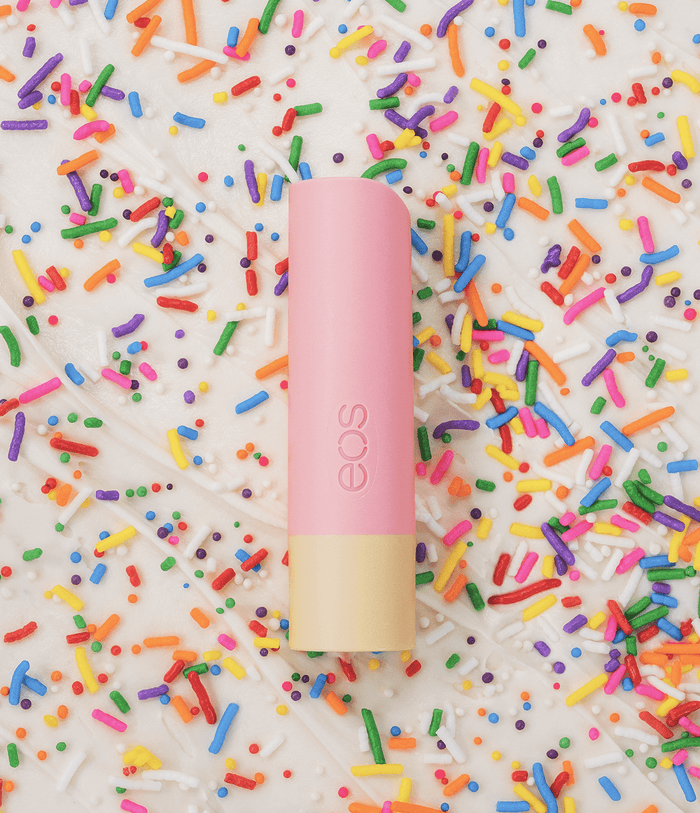 A pink and cream EOS lip balm tube standing upright on a white background covered in colorful sprinkles.
