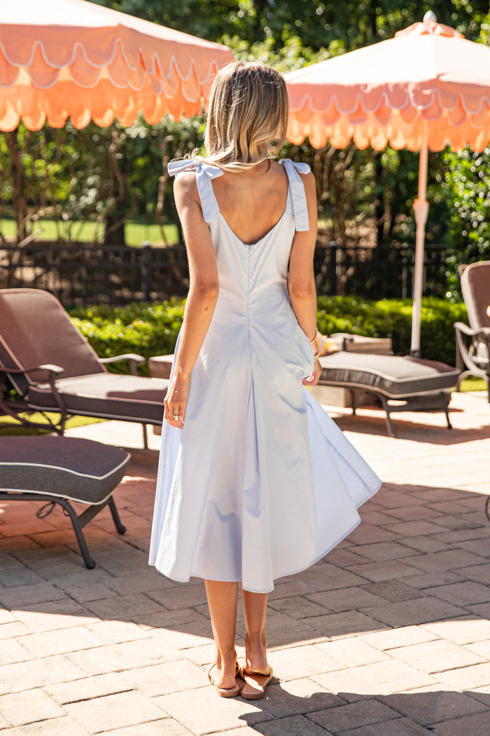 Woman in a light blue dress standing on a patio with orange umbrellas and lounge chairs.