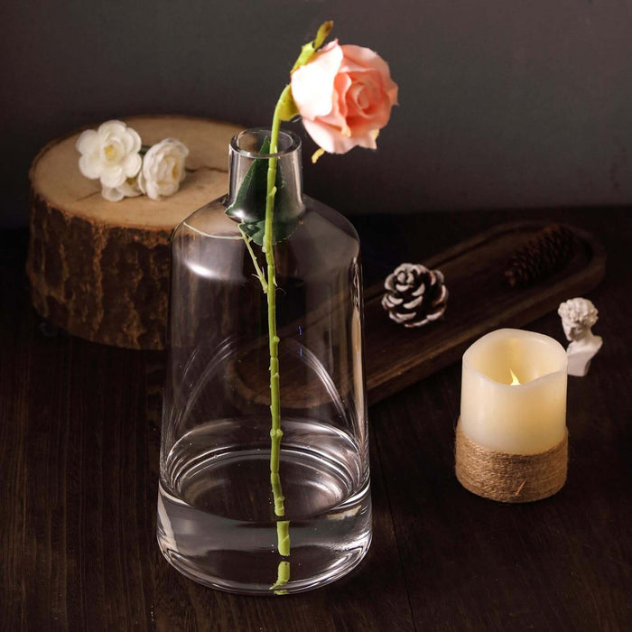 Glass vase with a rose and candle on a wooden table.