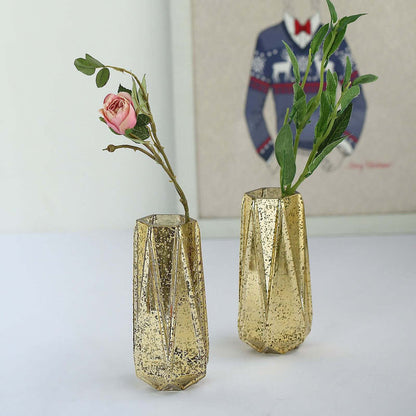 Gold geometric vases with flowers on a plain backdrop.