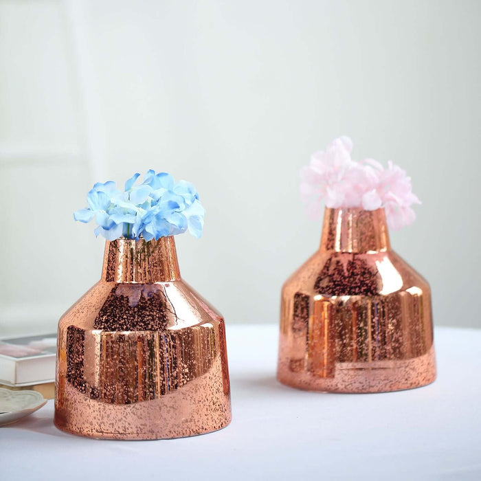 Copper vases with blue and pink flowers on a table.