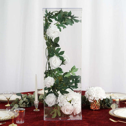 Clear acrylic vase with white roses and greenery, elegantly displayed on a table.