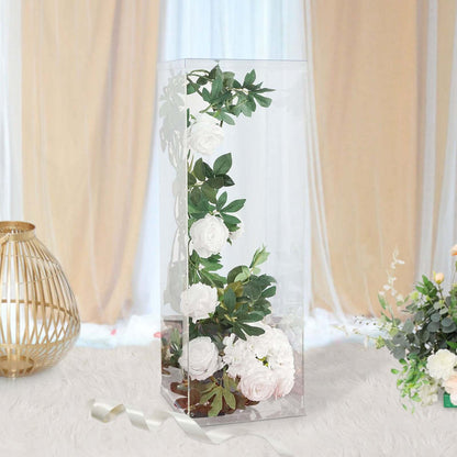 Floral arrangement in a clear display case with greenery and white roses.