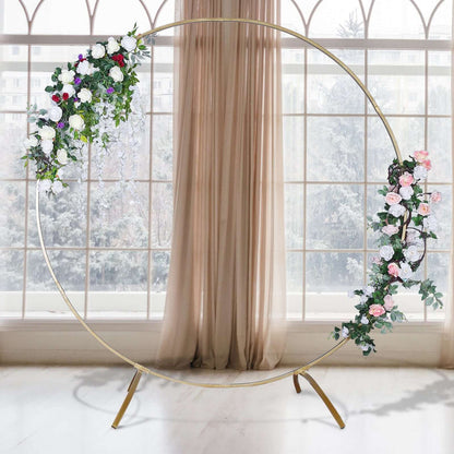 Floral wedding arch with gold frame and greenery against a window backdrop.