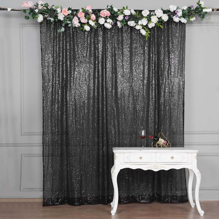 Black sequin curtain with floral garland above a white decorative table.