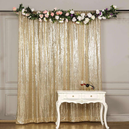 Gold sequin backdrop with floral garland and white table with wine bottle and glass.
