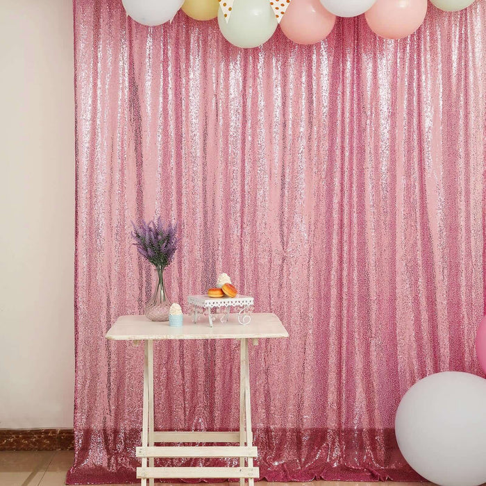 Pink sequin backdrop with balloons and a small table set for a celebration.
