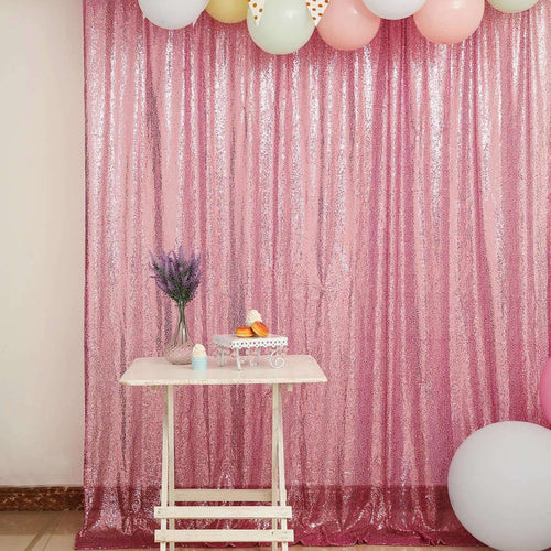 Pink sequin backdrop with balloons and a small table set for a celebration.