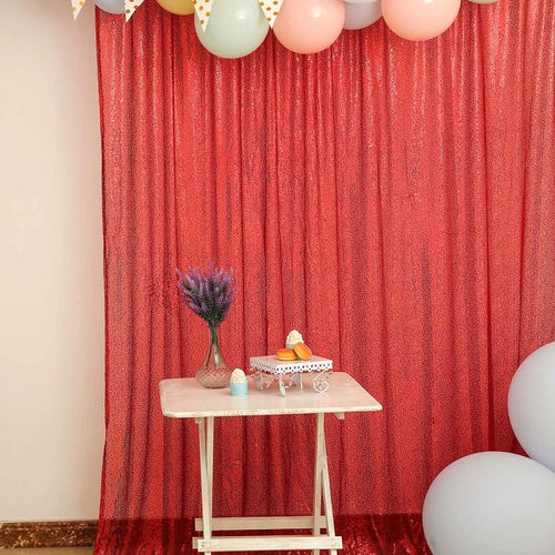 Decorative party setup with balloons, table, and flowers against a sparkling red backdrop.