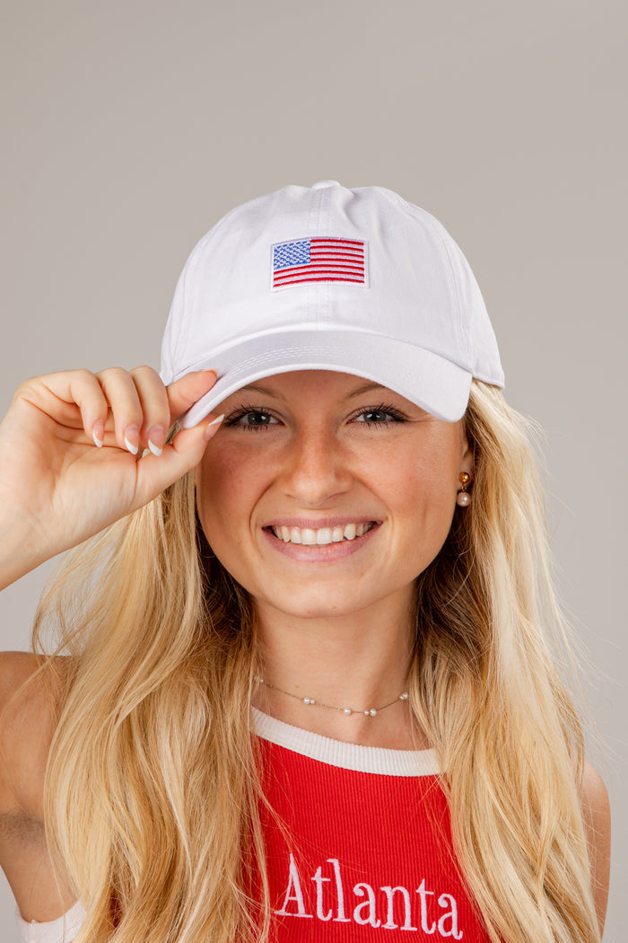Woman wearing a white cap with an American flag patch on a plain background