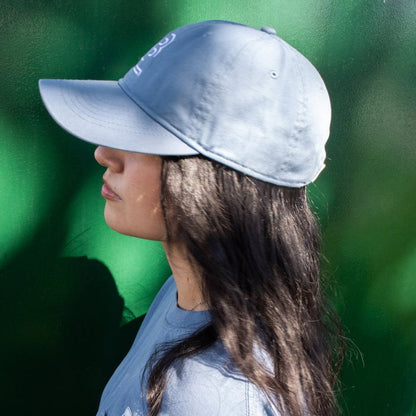 side profile of a woman wearing a blue baseball cap and blue t-shirt against a green background