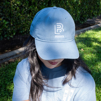 person sitting on the grass wearing a blue baseball cap with 'B' emblem stitched on the front and a matching blue t-shirt