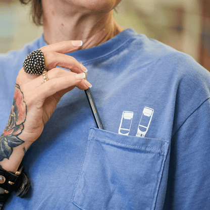 Person wearing a pocket tee with 2 white pencil graphics poking out of the chest pocket. A blackwing pencil is in the pocket.