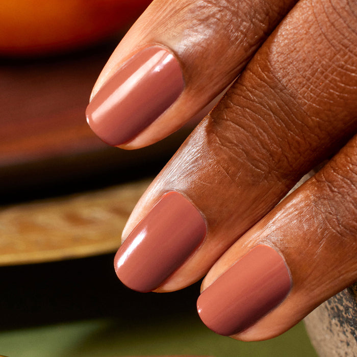 A close-up of a hand with medium to dark skin, featuring three neatly manicured nails painted in Manucurist’s Brique, a glossy shade beside muted mauve.