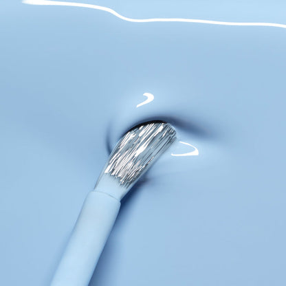 A close-up of a brush dipped in Manucurist's Bubble, a cool light blue LED Gel polish with grey undertones, creating a small swirl on the smooth surface.
