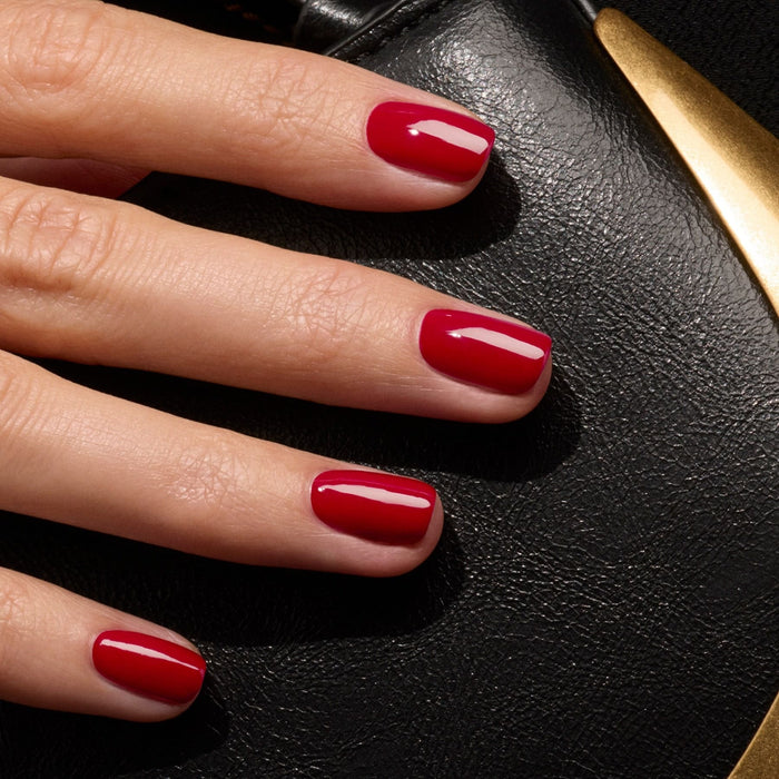 A hand with neatly manicured nails painted in Manucurist's Dark Dahlia from the Green™ range rests on textured black leather with a gold accent.
