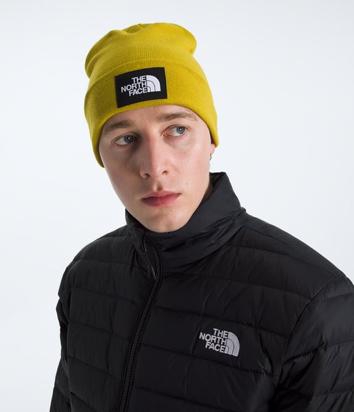 Person wearing a yellow beanie and black jacket with The North Face logo on a white background