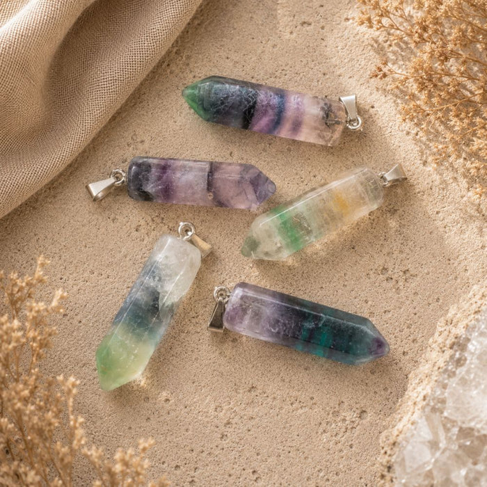 Fluorite point pendants displayed on a natural stone surface with soft linen and dried botanicals.