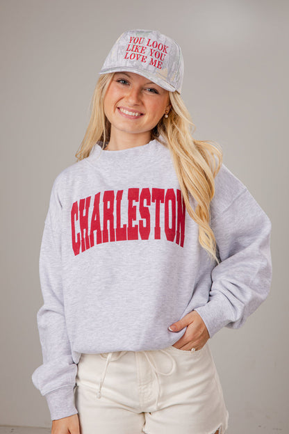 Person wearing a gray sweatshirt with 'Charleston' printed on it and a white cap.