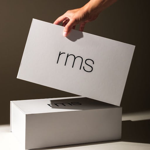 Hand holding the lid of a white Keepsake Gift Box with simple black "rms" logo on a clean, minimalist background, highlighting sustainable and recyclable packaging.