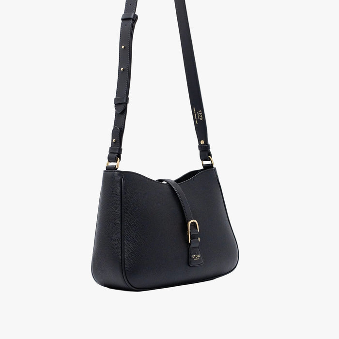 Off-axis view of STOW London's Beth bag and detachable crossbody strap in Black leather featuring gold stainless steel hardware on a white background