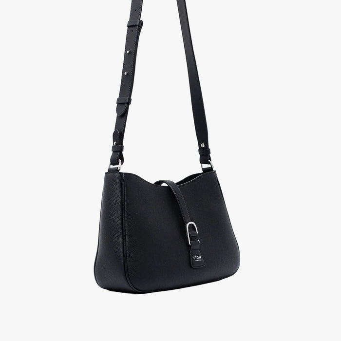 Off-axis view of STOW London's Beth bag and detachable crossbody strap in Black leather featuring silver stainless steel hardware on a white background