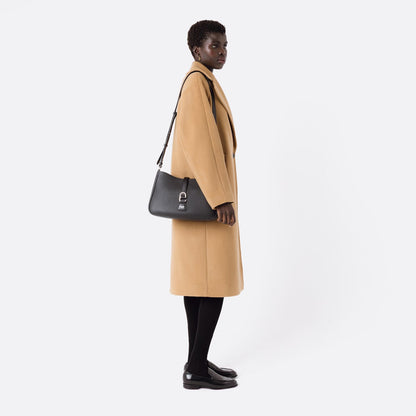 Model wearing STOW London's Beth bag with detachable crossbody strap in Black leather on her shoulder featuring silver stainless steel hardware on a white background