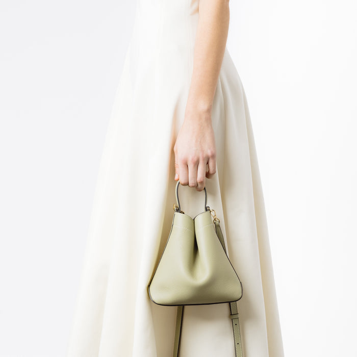 Model holding STOW London's Mini Curve in Pale Green pebbled leather with the detachable leather crossbody strap on a white background