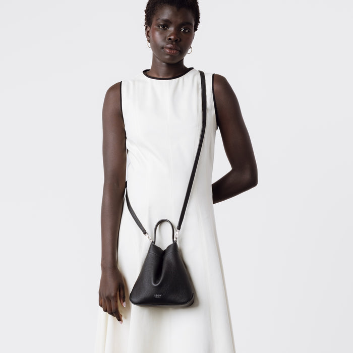 Model wearing STOW London's Mini Curve in Black pebbled leather with the detachable leather crossbody strap on a white background