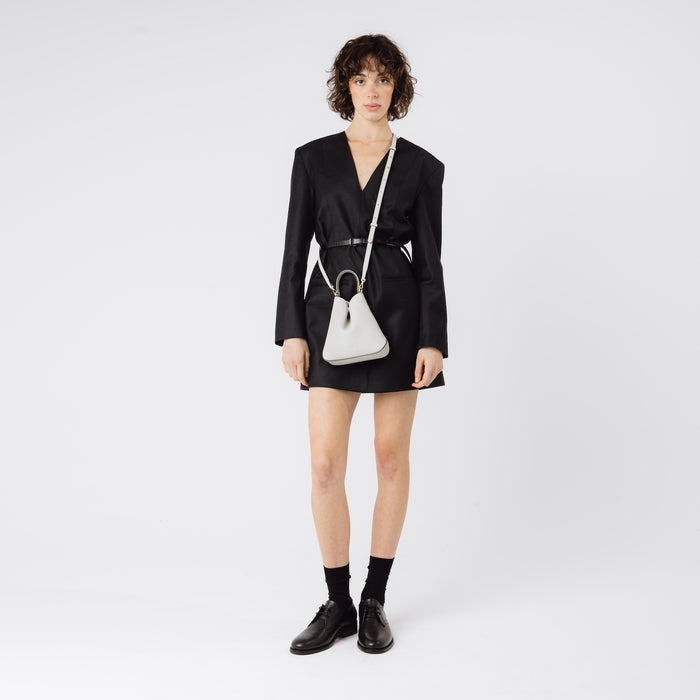 Model wearing STOW London's Mini Curve in Cloud Grey pebbled leather with the detachable leather crossbody strap on a white background