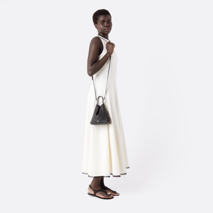 Model wearing STOW London's Mini Curve in Black pebbled leather with the detachable leather crossbody strap on her shoulder on a white background