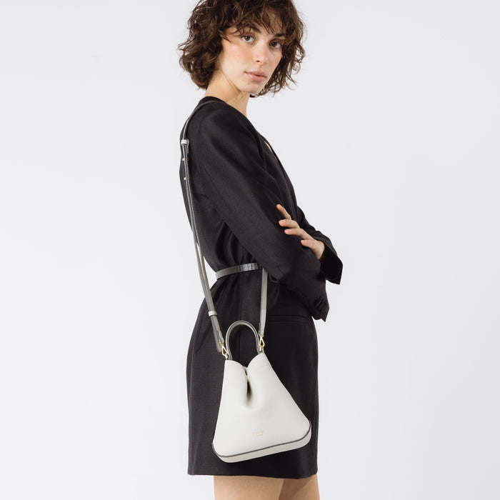 Model wearing STOW London's Mini Curve in Cloud Grey pebbled leather with the detachable leather crossbody strap on her shoulder on a white background
