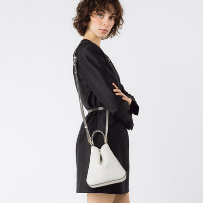 Model wearing STOW London's Mini Curve in Cloud Grey pebbled leather with the detachable leather crossbody strap on her shoulder on a white background