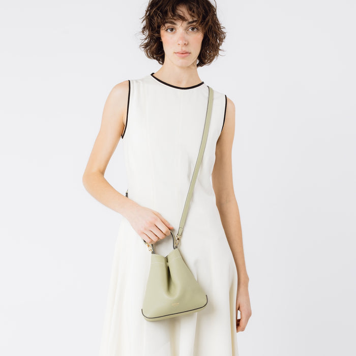 Model wearing STOW London's Mini Curve in Pale green pebbled leather with the detachable leather crossbody strap on a white background
