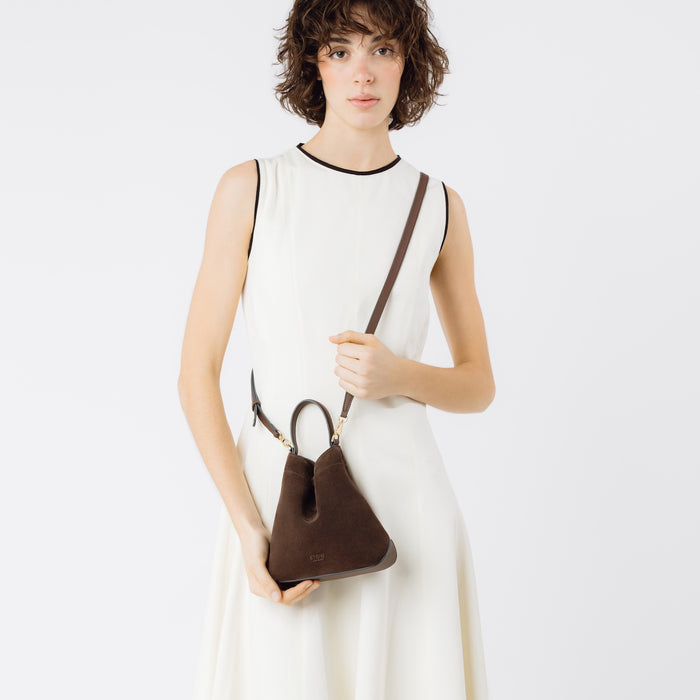 Model holding STOW London's Mini Curve in Chocolate suede leather crossbody by the detachable full leather strap