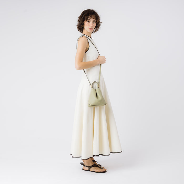 Model wearing STOW London's Mini Curve in Pale Green pebbled leather with the detachable leather crossbody strap on her shoulder on a white background