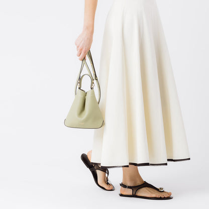 Model holding  STOW London's Mini Curve in Pale Green pebbled leather by the detachable leather crossbody strap at her side on a white background