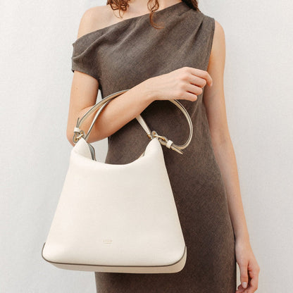 Model wearing STOW London's Curve in Spring Moon leather featuring the detachable shoulder strap and top handle with gold hardware and details
