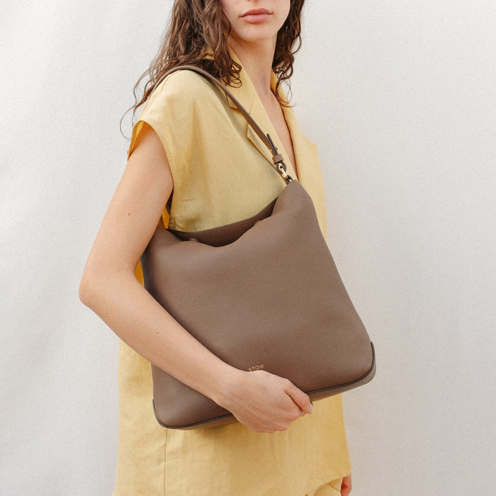 Model wearing STOW London's Curve in Mocha leather featuring the detachable shoulder strap with gold hardware and details