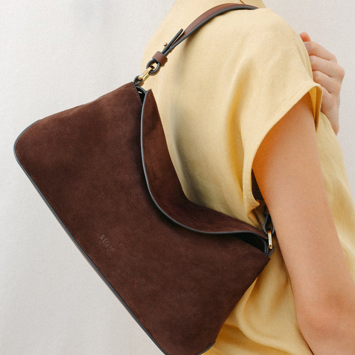 Model wearing STOW London's East West in Chocolate suede leather featuring the detachable shoulder strap with gold hardware