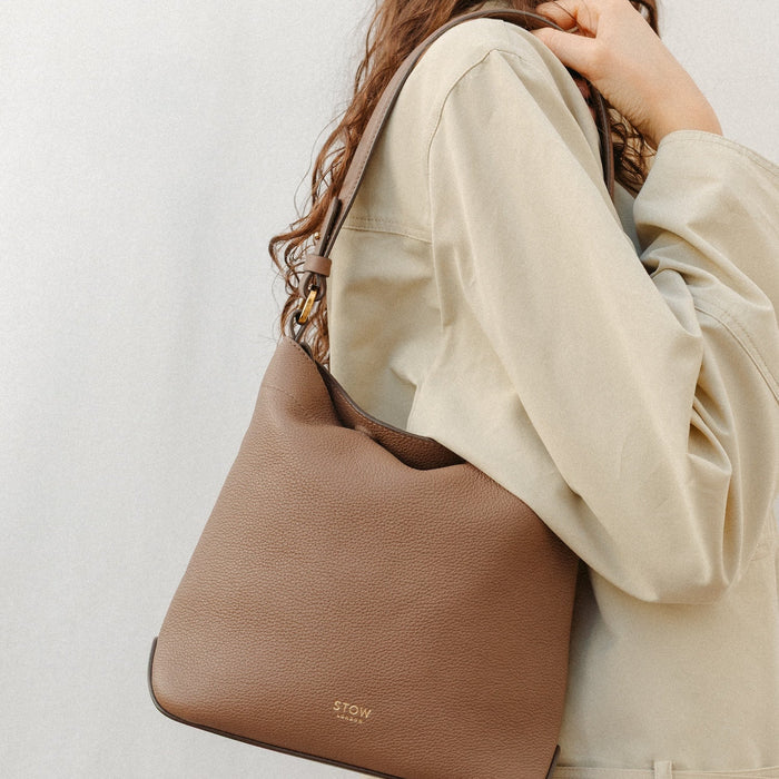 Model wearing STOW London's Midi Curve in Mocha leather featuring the detachable shoulder strap with gold hardware and details