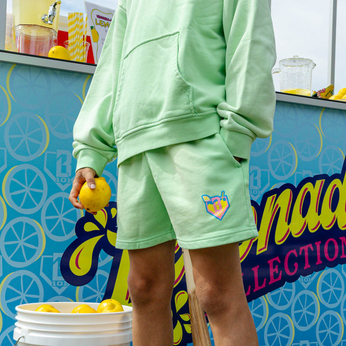 Youth model wearing green youth shorts with "Lemonade" design
