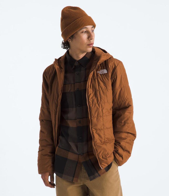 Person wearing a brown jacket and beanie with a visible brand logo on a white background