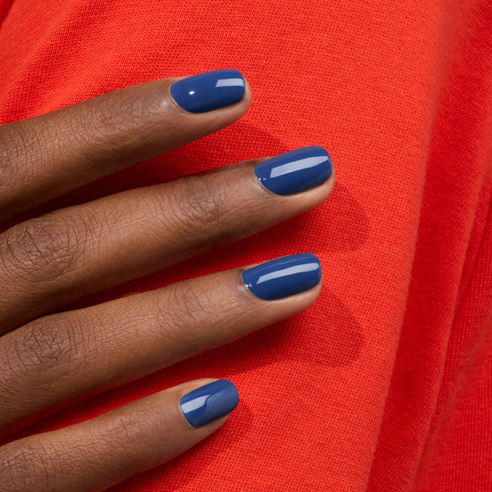 A hand with neatly manicured nails painted in Manucurist’s "Midnight" gel polish rests against bright red fabric.
