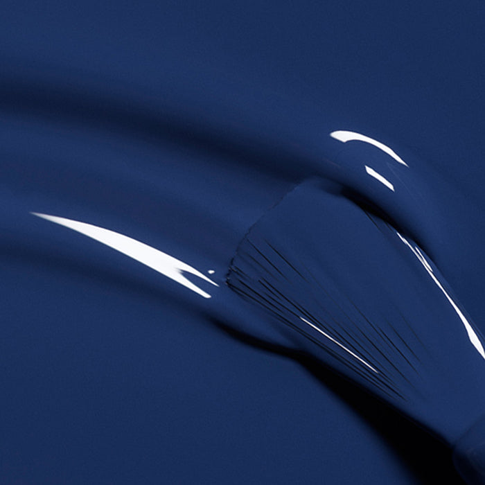 A close-up shows a paintbrush applying Manucurist’s Midnight gel polish, its glossy, midnight blue finish reflecting light off the smooth surface.