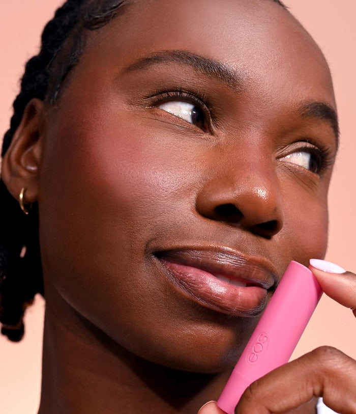 Woman applying pink lip balm with a neutral background