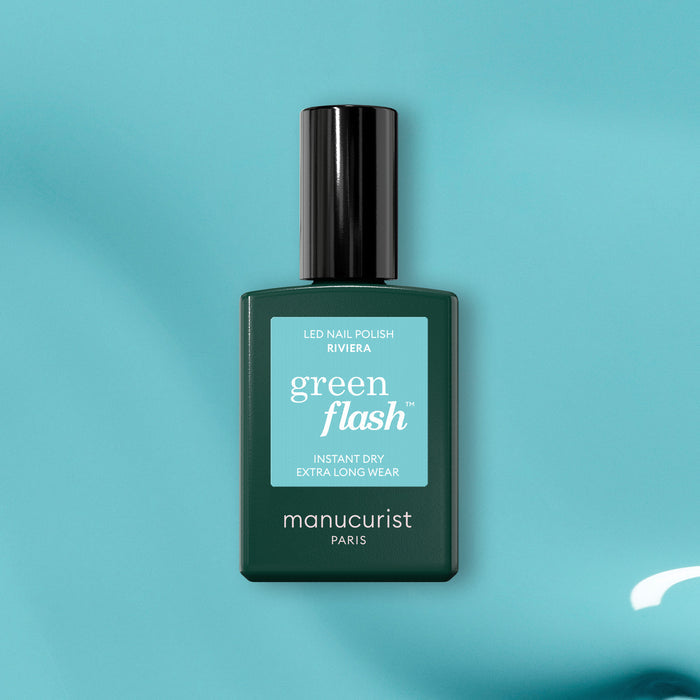 A green bottle of Manucurist Riviera gel polish rests on a teal surface, displaying its Instant Dry and Extra Long Wear features.