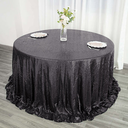 Black sequin tablecloth on round table with floral centerpiece and plates.