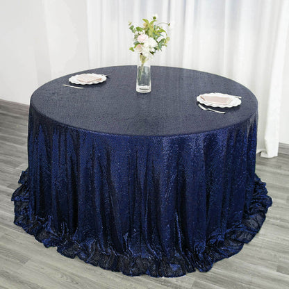 Navy blue sequin tablecloth on round table with floral centerpiece and plates.